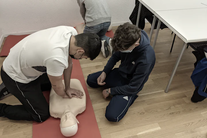 Deux stagiaires agenouillés en salle de cours, l’un pratiquant un massage cardiaque sur un mannequin posé sur un tapis.